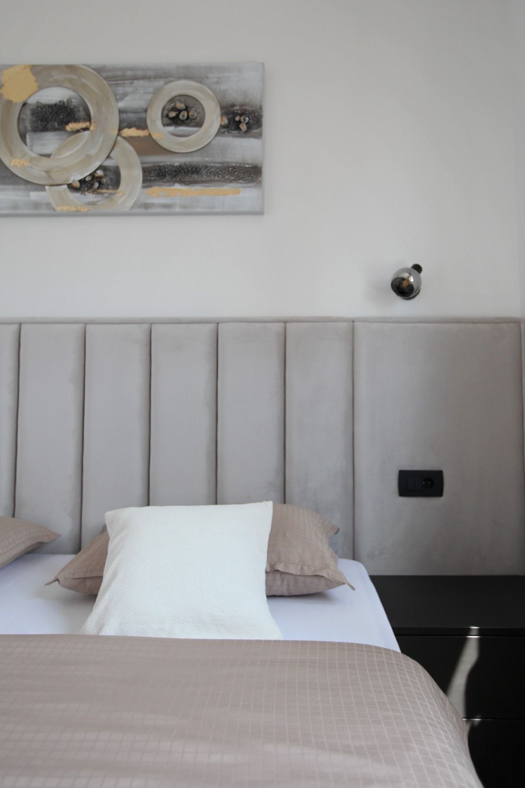 A bedroom with a bed, pillows, a headboard, a nightstand, and a wall-mounted light fixture.