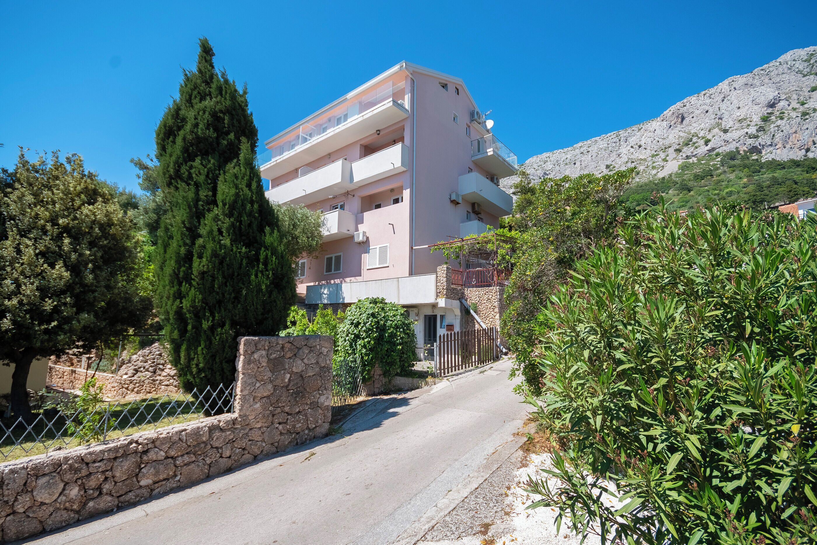 A multi-story building with balconies, a stone wall, and a mountain in the background.