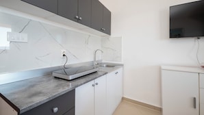 A modern kitchen with grey cabinets, a marble backsplash, a built-in oven, and a flat-screen TV mounted on the wall. - Apartments Zvonko (Omis)