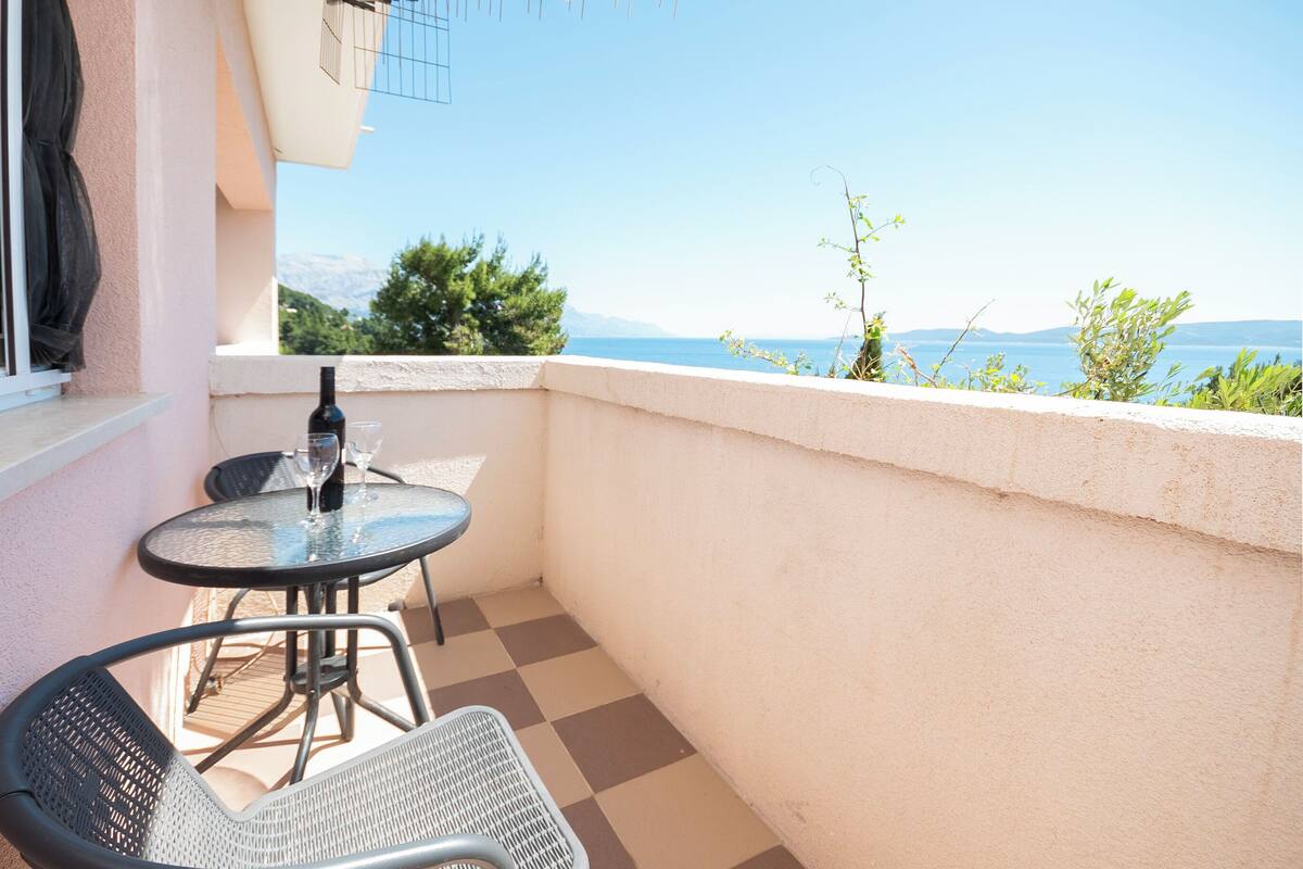 A balcony with a checkered floor, a table, two chairs, a bottle, and a glass.