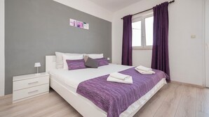 A modern bedroom with a large bed, white nightstands, a grey accent wall, and purple curtains. - Apartments Zvonko (Omis)