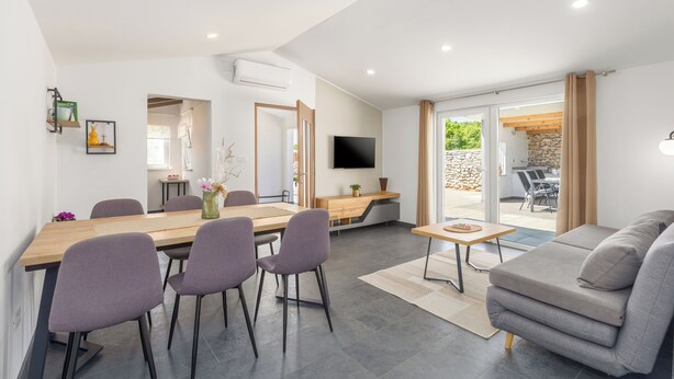A modern living room with a sofa, a dining table with chairs, a TV mounted on the wall, and a view of the outdoors. - House Prenc (Sveti Petar u Sumi)