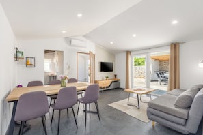 A modern living room with a sofa, a dining table with chairs, a TV mounted on the wall, and a view of the outdoors. - House Prenc (Sveti Petar u Sumi)