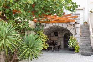 An outdoor patio area with a stone archway, a wooden pergola, and a dining table set. - House Punat Residence (Punat)
