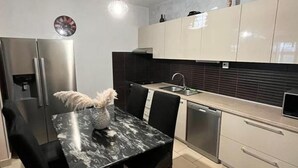 A modern kitchen with a marble countertop, black chairs, a stainless steel refrigerator, and a pendant light. - Apartment Ivana (Makarska)