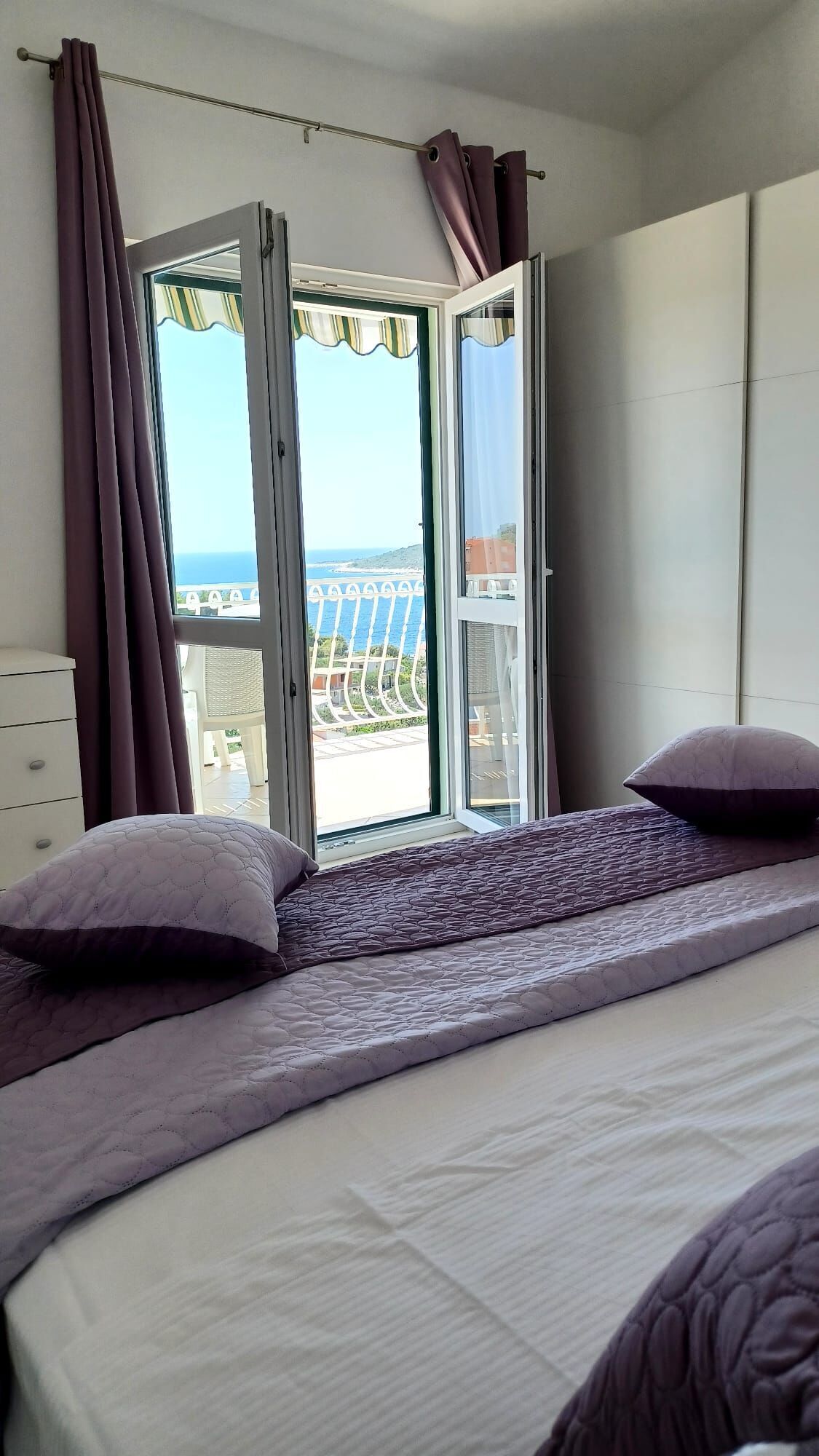 Een slaapkamer met een bed, een dressoir en uitzicht op zee door een open deur.
