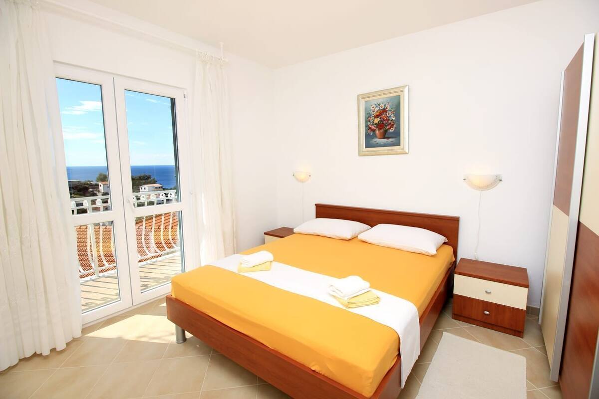 A hotel room with a bed, a nightstand, a lamp, a painting, and a balcony with a view.
