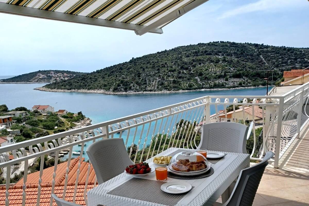 A terrace with a table set for breakfast overlooking a coastal landscape.