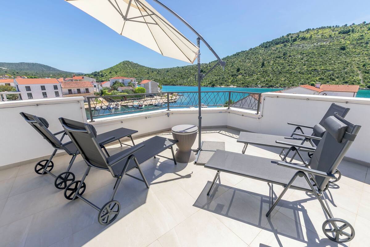 Eine Dachterrasse mit Außenmöbeln, Blick auf das Meer und einem Bergpanorama.