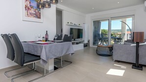 Uma área de refeições moderna com uma mesa posta para dois, uma TV de tela plana e uma varanda com assentos externos.