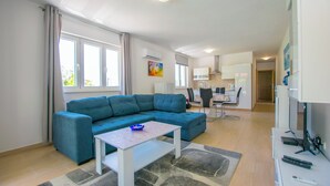 Una sala de estar moderna con un sofá seccional azul, una mesa de centro blanca y una cocina al fondo.
