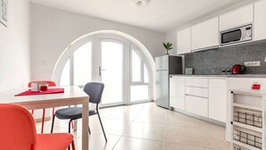 A modern kitchen with white cabinets, a microwave, and a coffee maker. There is a dining area with a table and chairs. - Apartment Sweet Studio (Punat)