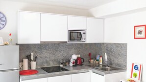 A compact kitchen with white cabinets, a built-in microwave, a sink, and a countertop with various kitchen items. - Apartment Sweet Studio (Punat)