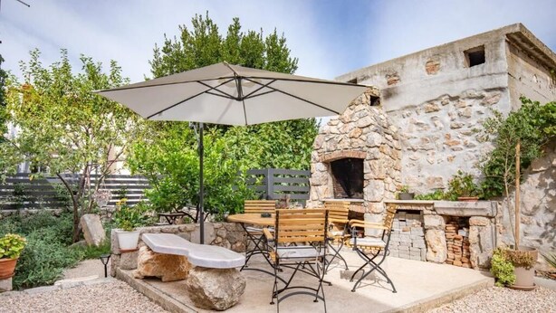 An outdoor patio with a stone-built oven, wooden furniture, and a large umbrella. - Apartment Sweet Studio (Punat)