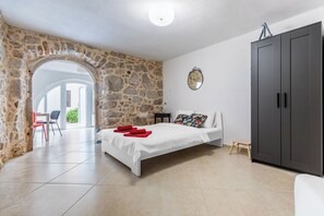 A bedroom with a stone wall, a bed, a wardrobe, and a small table with a mirror. - Apartment Sweet Studio (Punat)