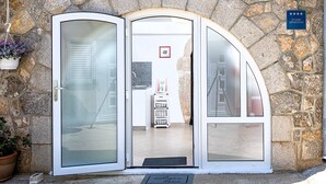 A stone facade with a glass door entrance, a sign indicating a studio apartment, and a small indoor area with a sink and a framed picture on the wall. - Apartment Sweet Studio (Punat)