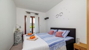 A bedroom with a bed, a bedside table, a lamp, a window with curtains, and a wall decoration. - Apartment M&M (Lopar)