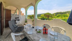 A terrace with a table set for dining, white chairs, a hanging chair, and a view of green hills. - Apartment M&M (Lopar)