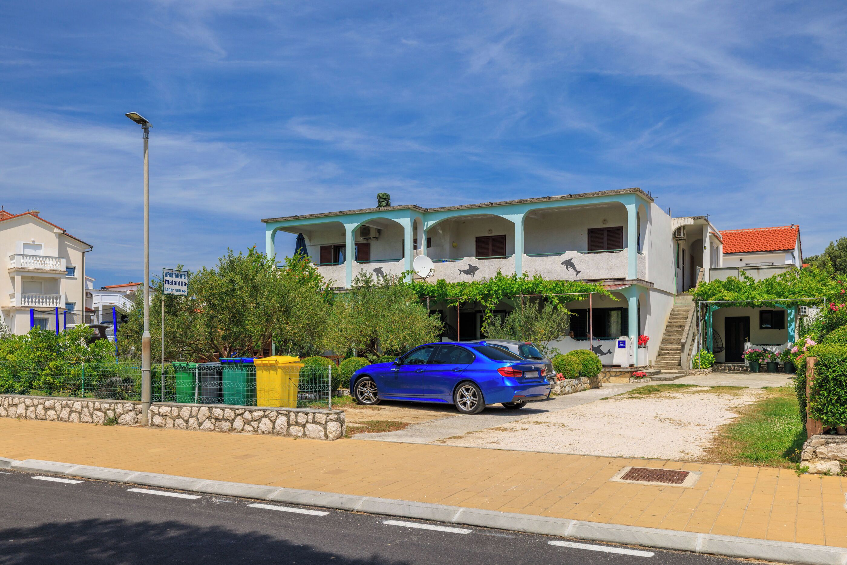 A two-story building with a balcony, a car parked in front, and a clear sky.