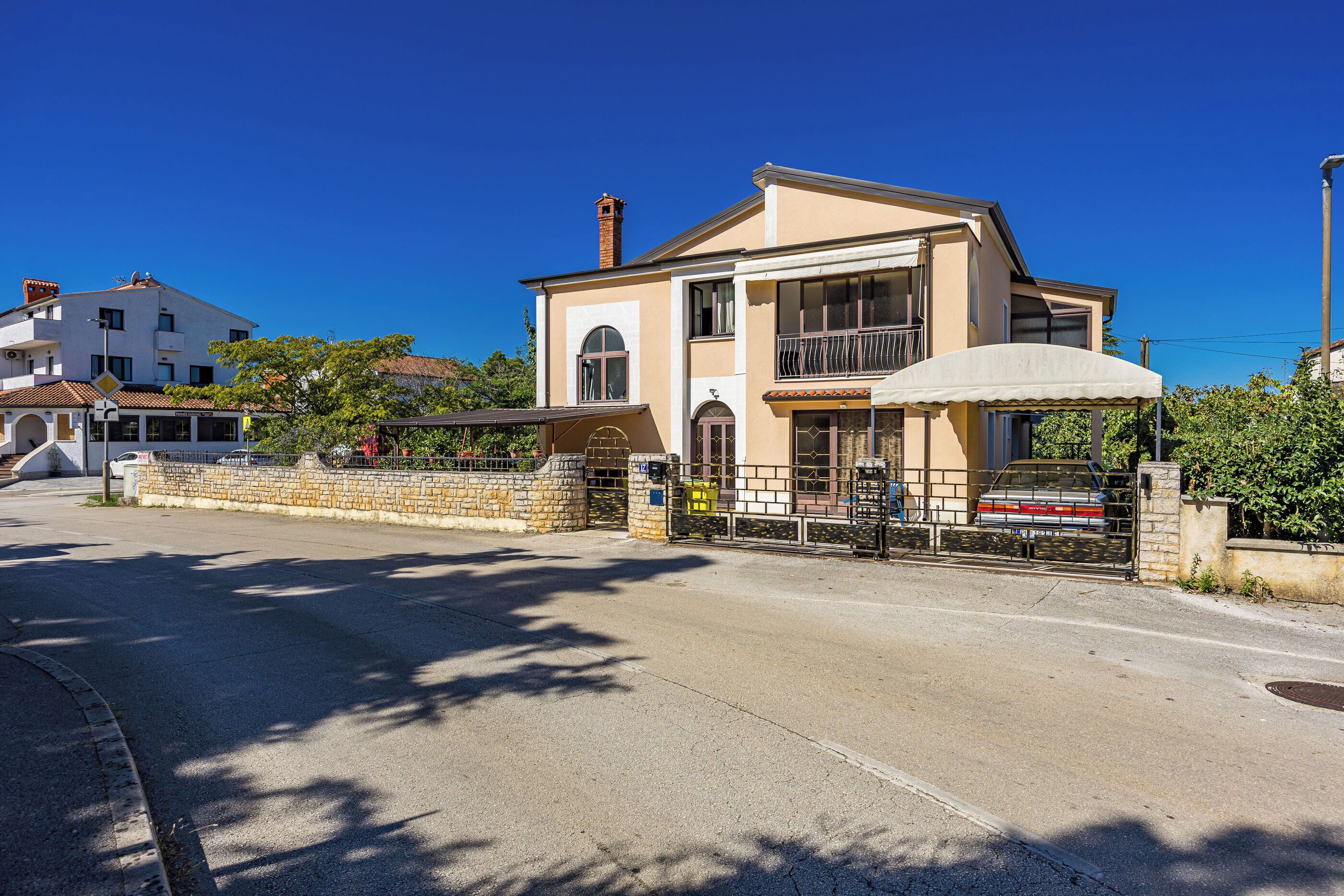 Une maison à deux étages avec un mur en pierre et une entrée fermée par un portail.