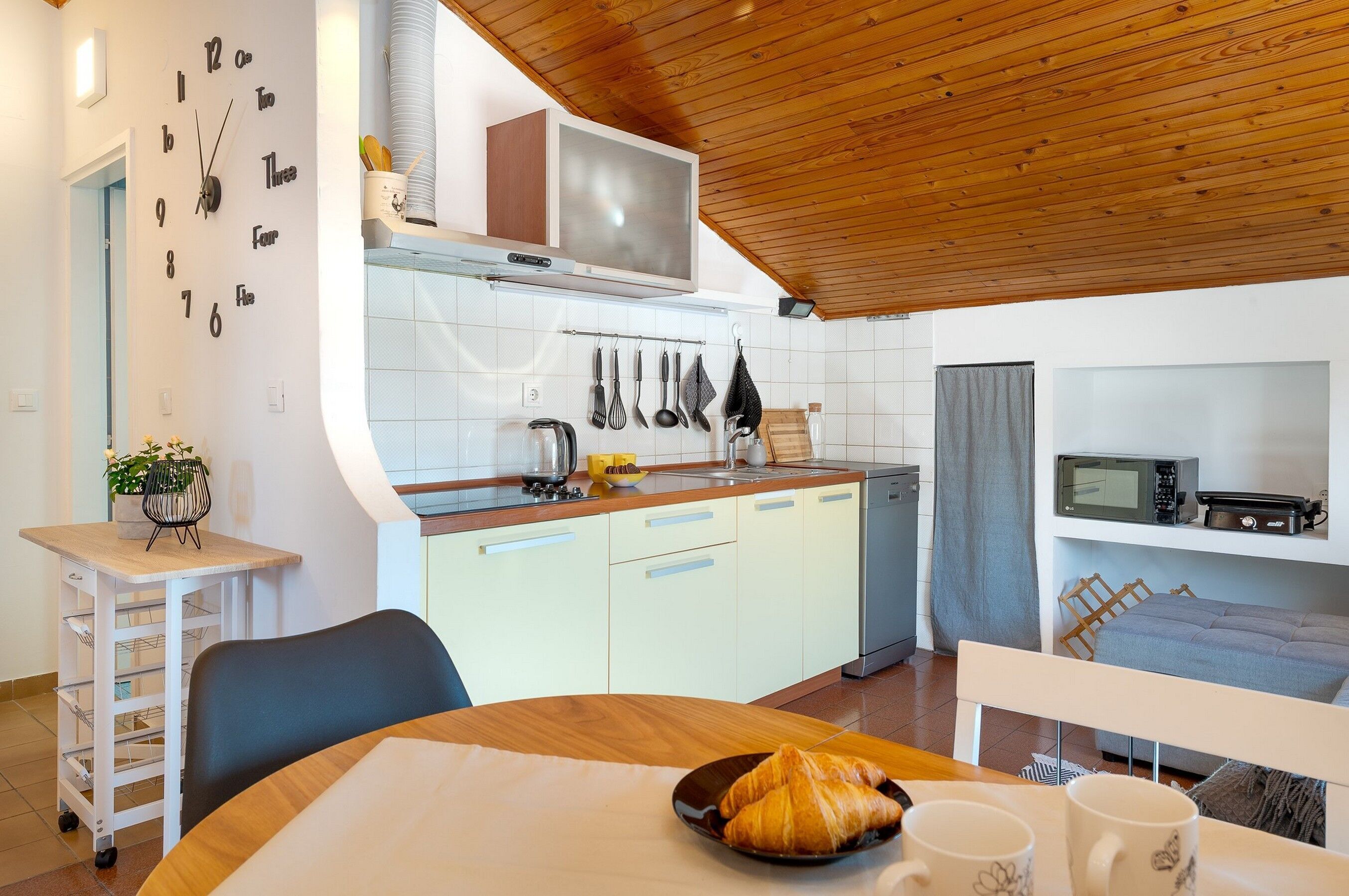 A modern kitchen with white cabinets, a wooden ceiling, and a dining area with a table set for two.