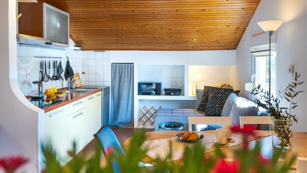 Eine moderne Küche mit Holzbalkendecke, weißen Schränken und einem Essbereich mit Tisch für zwei Personen.