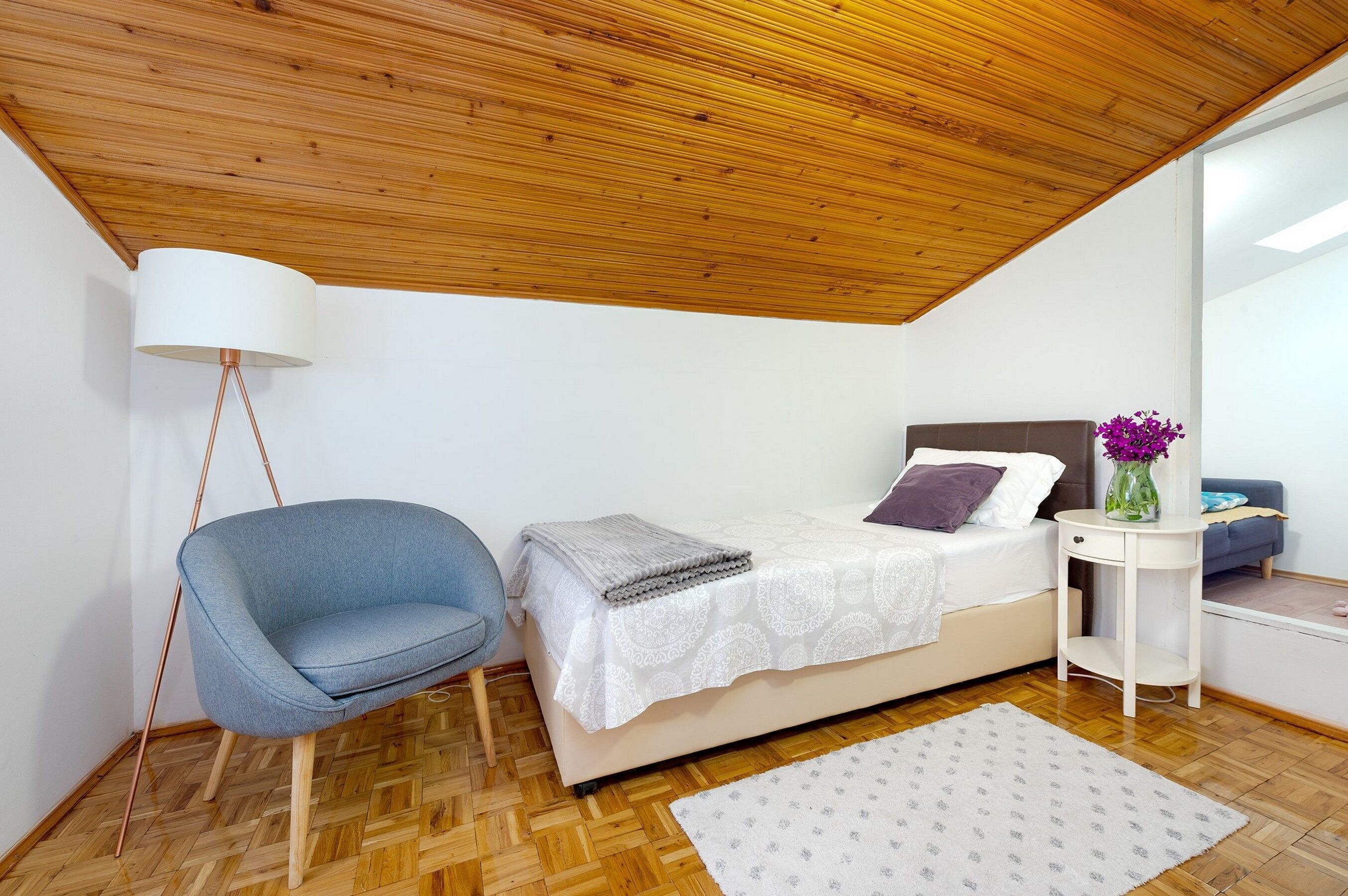 Una camera da letto con un letto, una sedia, un comodino, una lampada e un tavolino con un vaso.