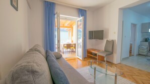 Ein modernes Wohnzimmer mit einem grauen Sofa, einem Glastisch und einem an der Wand montierten Fernseher.