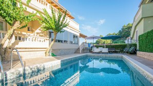 Ein Schwimmbecken mit Fliesenrand, einer Metallleiter und einer kleinen Terrasse mit Tisch und Stühlen.