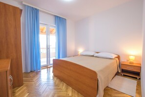 Ένα υπνοδωμάτιο με ένα ξύλινο κρεβάτι, ένα κομοδίνο με ένα φωτιστικό και θέα που διακρίνεται μέσα από μια γυάλινη πόρτα.