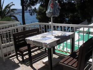 A balcony with a table covered by a newspaper, two wooden benches, and a view of the sea and a bridge. - Apartments Alice Seafront (Slivno)