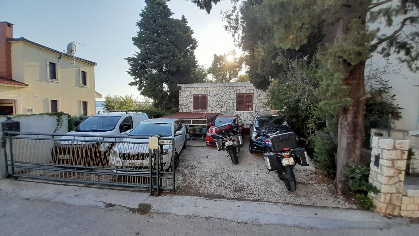 A residential driveway with parked cars and motorcycles, a stone wall, and a gate.