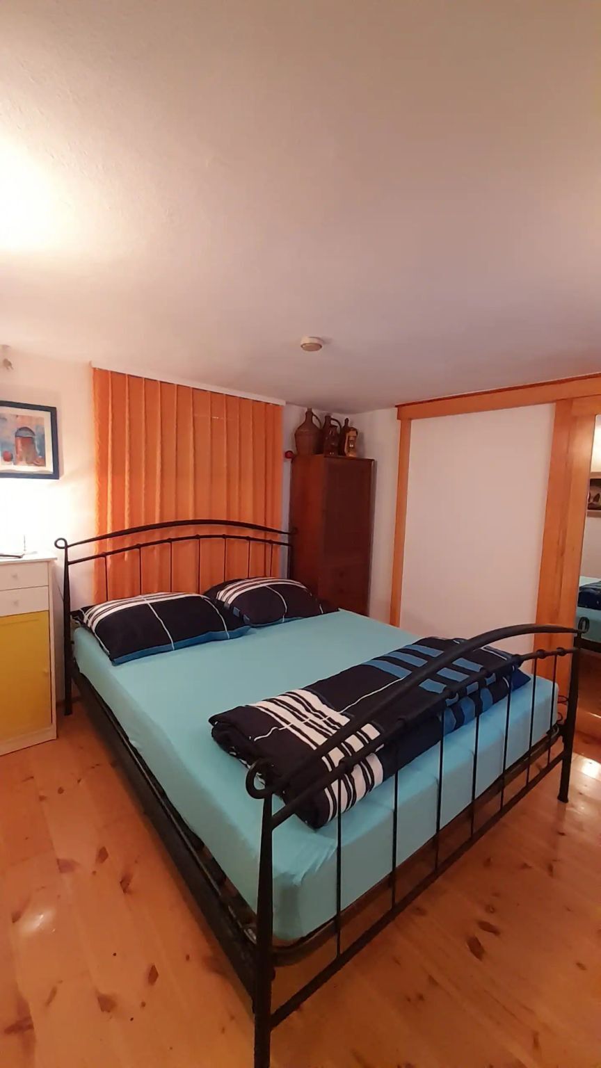 Ein Zimmer mit einem Einzelbett, einem Metallgestell, einer hellblauen Matratze und gestreiften Kissen.
