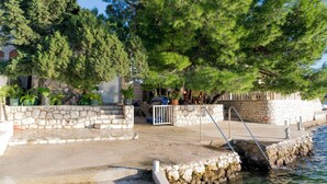 Μια πέτρινη σκάλα που οδηγεί σε μια πέτρινη πλατφόρμα δίπλα στο νερό, με ένα μεταλλικό κιγκλίδωμα και μια μικρή βάρκα αγκυροβολημένη κοντά.