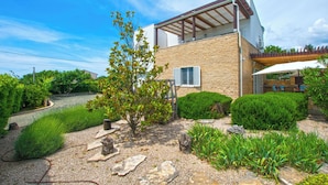 A modern two-story house with a stone facade, a covered patio, and a well-maintained garden with various plants and a small tree. - House Srecko (Polaca)