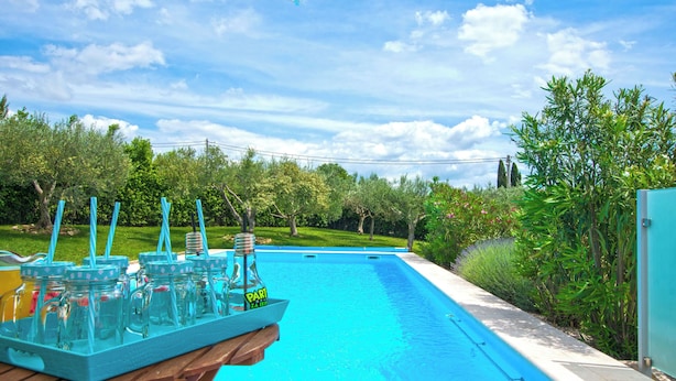 A swimming pool with a wooden deck and a table holding glass jars with straws. - House Srecko (Polaca)