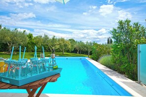 Una piscina con un prendisole in legno e un tavolo su cui ci sono vasetti di vetro con cannucce.
