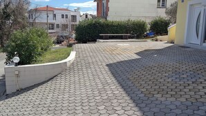 A paved courtyard with a white wall, a bench, and a small garden area. - Apartment Sarah (Cavle)