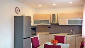 A modern kitchen with a refrigerator, oven, microwave, and sink. There is a dining table with chairs and a bowl of fruit. - Apartment Sarah (Cavle)