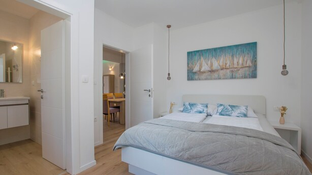 Et soveværelse med seng, et natbord, et maleri og et skrivebord med stole.