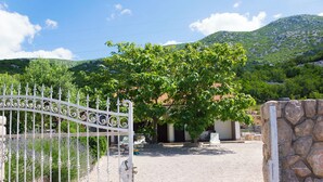 Un ingresso recintato con cancello in metallo, un muro di pietra e un albero sullo sfondo.