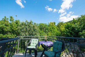 Uma varanda com duas cadeiras e uma mesa, com vista para uma floresta verdejante.