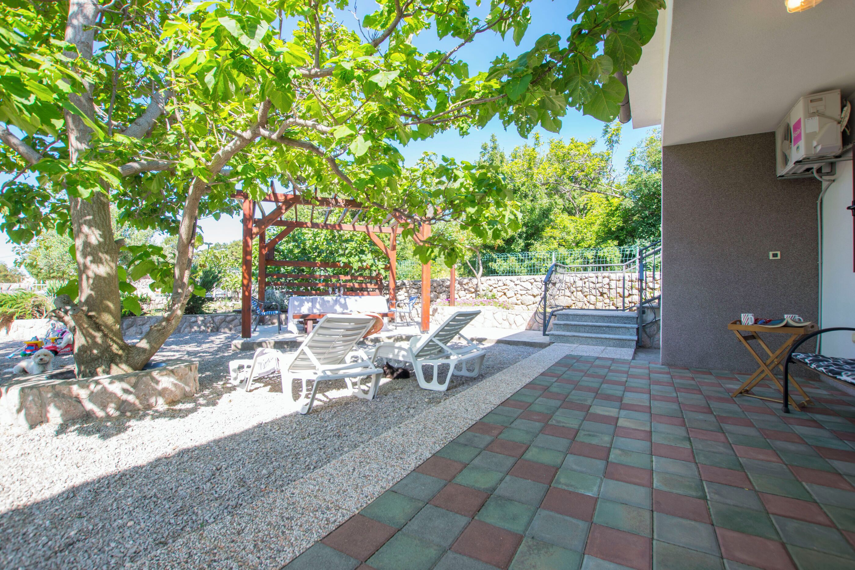 Een overdekt terras met een pergola, buitenmeubels en een grindpad.