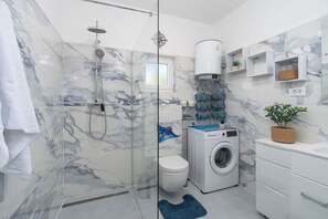 A modern bathroom with a glass-enclosed shower, a washing machine, and marble-patterned walls. - House Adriatic Blue Dream (Razanac)