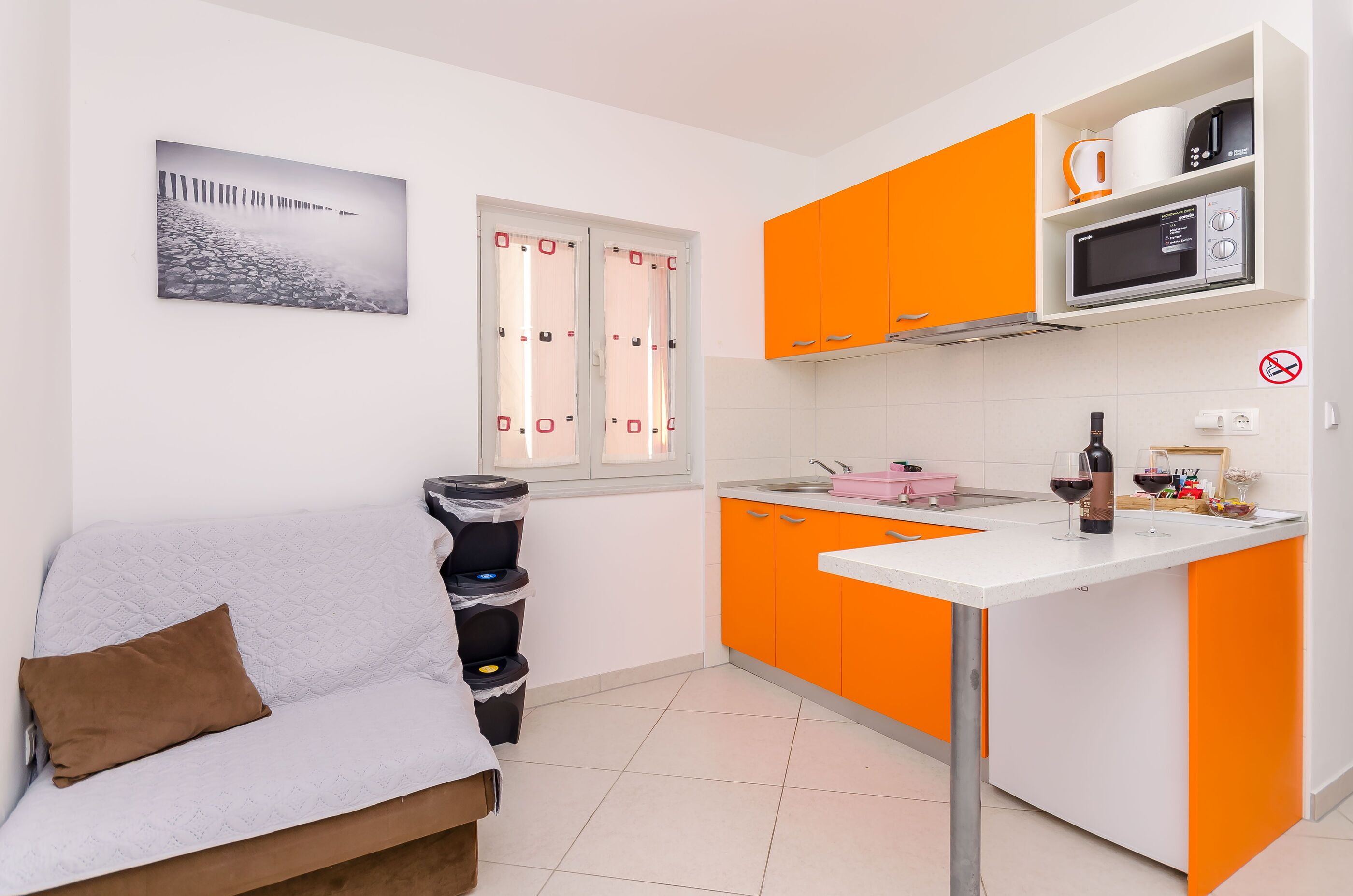 Een kleine keuken met oranje kastjes, een wit aanrecht en een eethoekje.