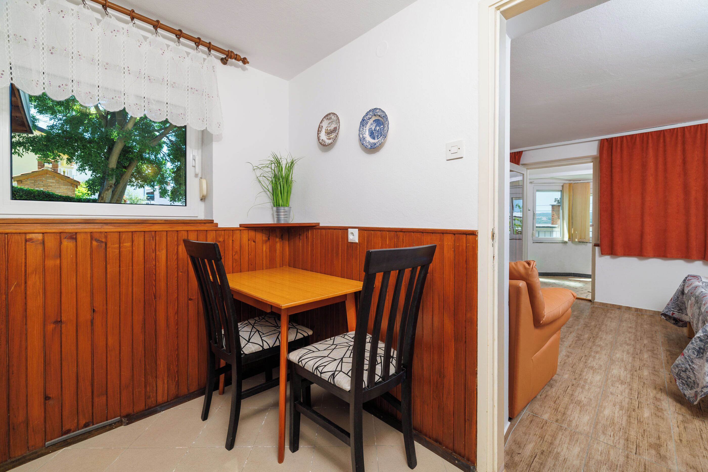 A dining area with a wooden table and chairs, a window with a view of a tree, and two decorative plates on the wall.