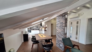 A modern kitchen with a brick accent wall, a dining area with a wooden table and chairs, and a loft bedroom with a sloped ceiling. - Apartments Mar (Crikvenica)