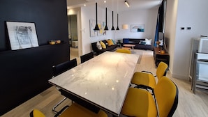 A modern living room with a dining area, featuring a marble table, yellow chairs, a dark sofa, and artwork on the walls. - Apartments Mar (Crikvenica)