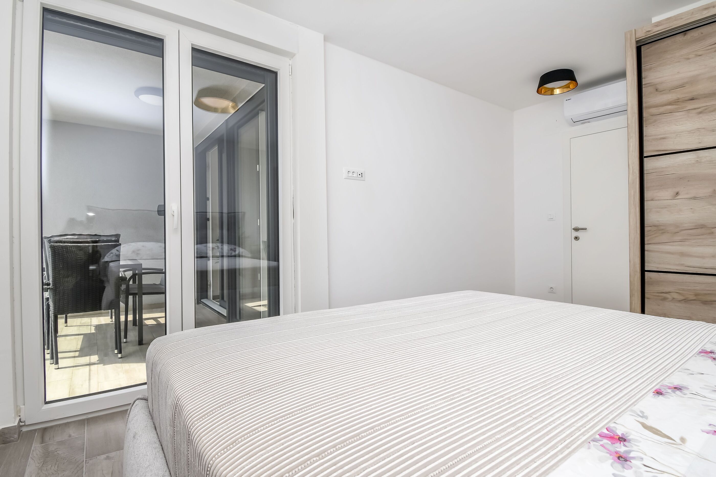 Un dormitorio con cama, puerta corrediza de vidrio a un balcón, armario y equipo de aire acondicionado.