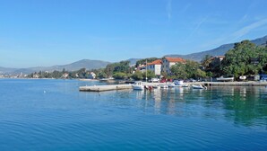A calm waterfront with boats docked, a pier, and buildings in the background. - Apartments Castel L (Kastela)